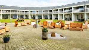 A courtyard with wooden furniture and a building with multiple balconies. - Sondervig Holiday Center (Ringkobing)