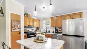 A modern kitchen with wooden cabinets, a stainless steel refrigerator, a marble island, and pendant lighting. - Brand new listing!!! Relax and unwind at this stunning Northwoods pool house featuring a private in-ground pool, fire pit, patio, garage space, and sleeping for 11 guests! (Mountain)
