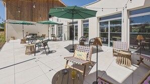 Un patio al aire libre con varias zonas de estar, que incluyen sillas y mesas, bajo sombrillas.