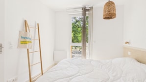 Un dormitorio con una cama grande, una escalera de madera, una lámpara colgante de mimbre y vistas al exterior.
