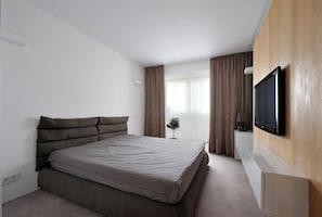 Ein modernes Schlafzimmer mit einem Bett, einem an der Wand montierten Fernseher und einem Fenster mit VorhÀngen.