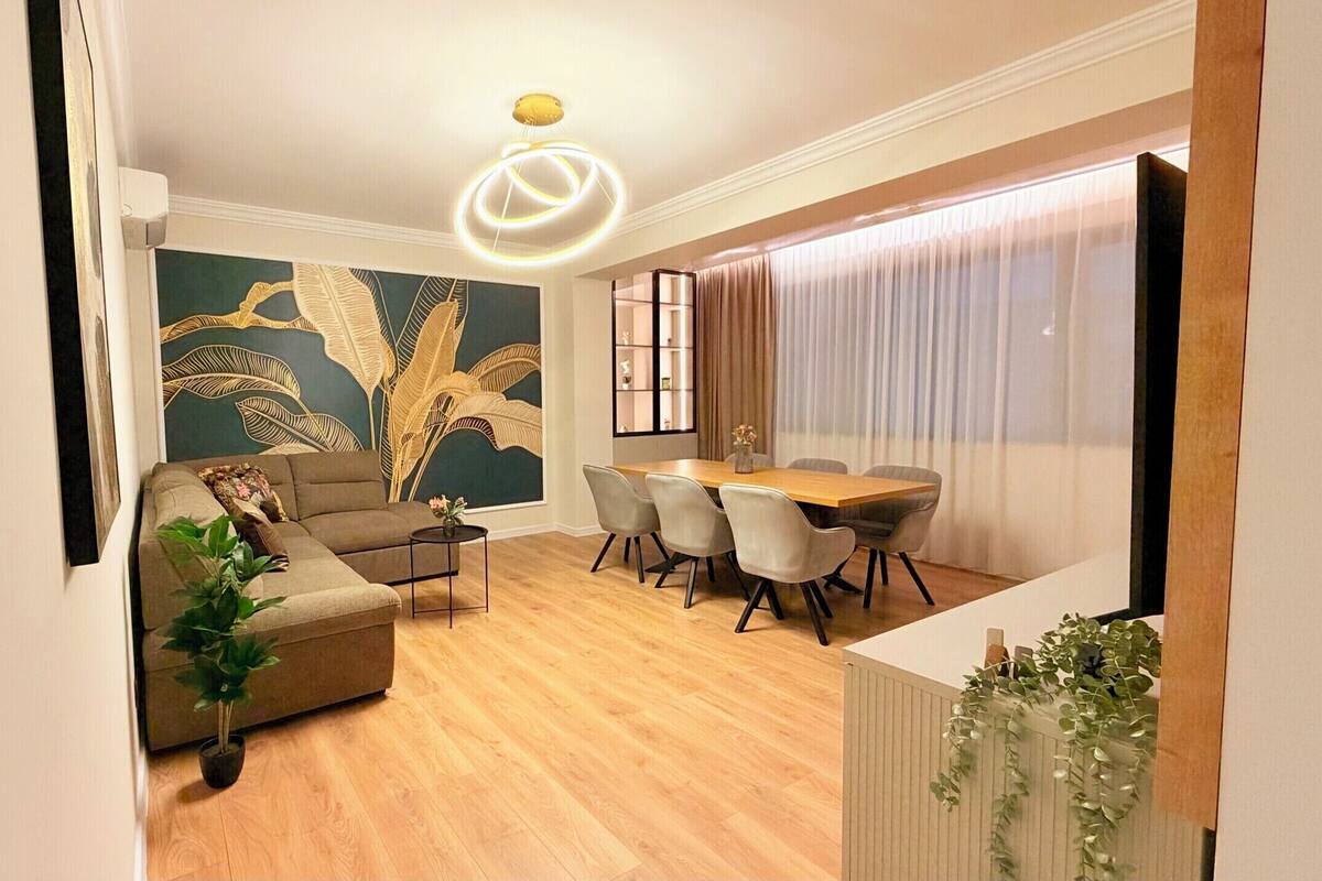A modern living room with a sofa, dining table, chairs, and a decorative wall.