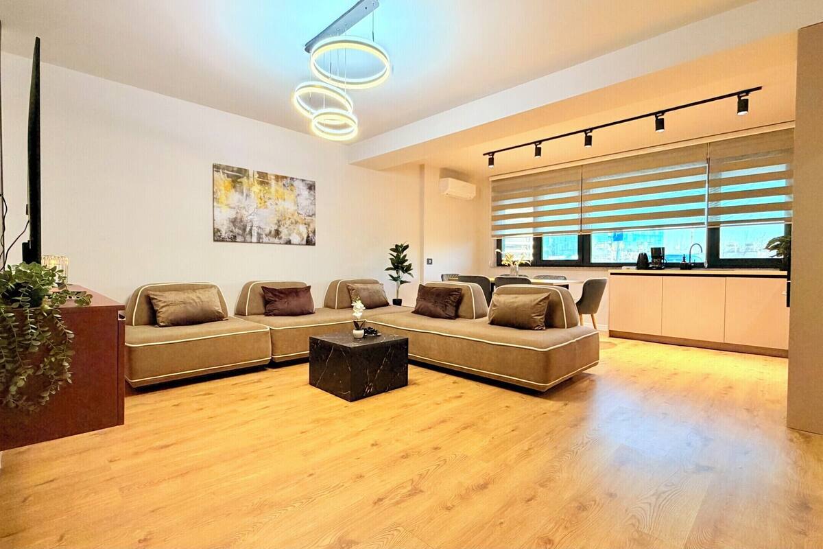 A modern living room with a sectional sofa, a marble coffee table, and a large window with blinds.
