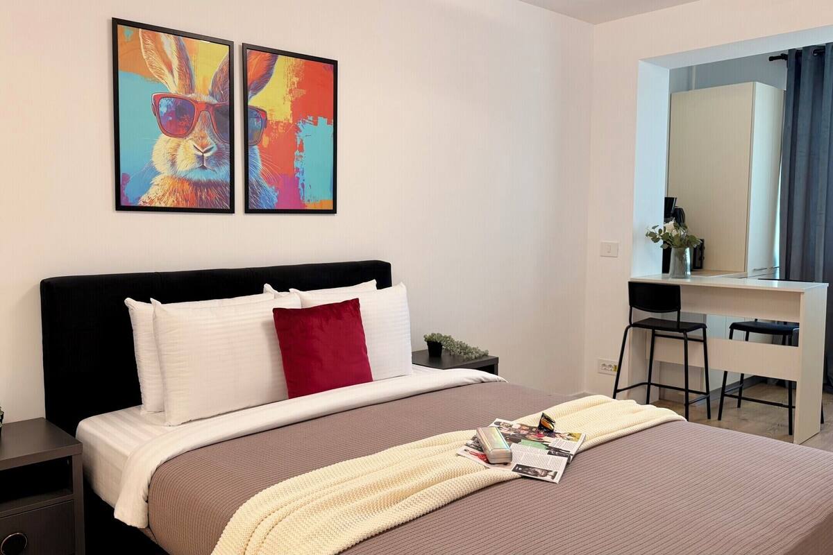 A modern hotel room with a bed, a desk, and a mirror.