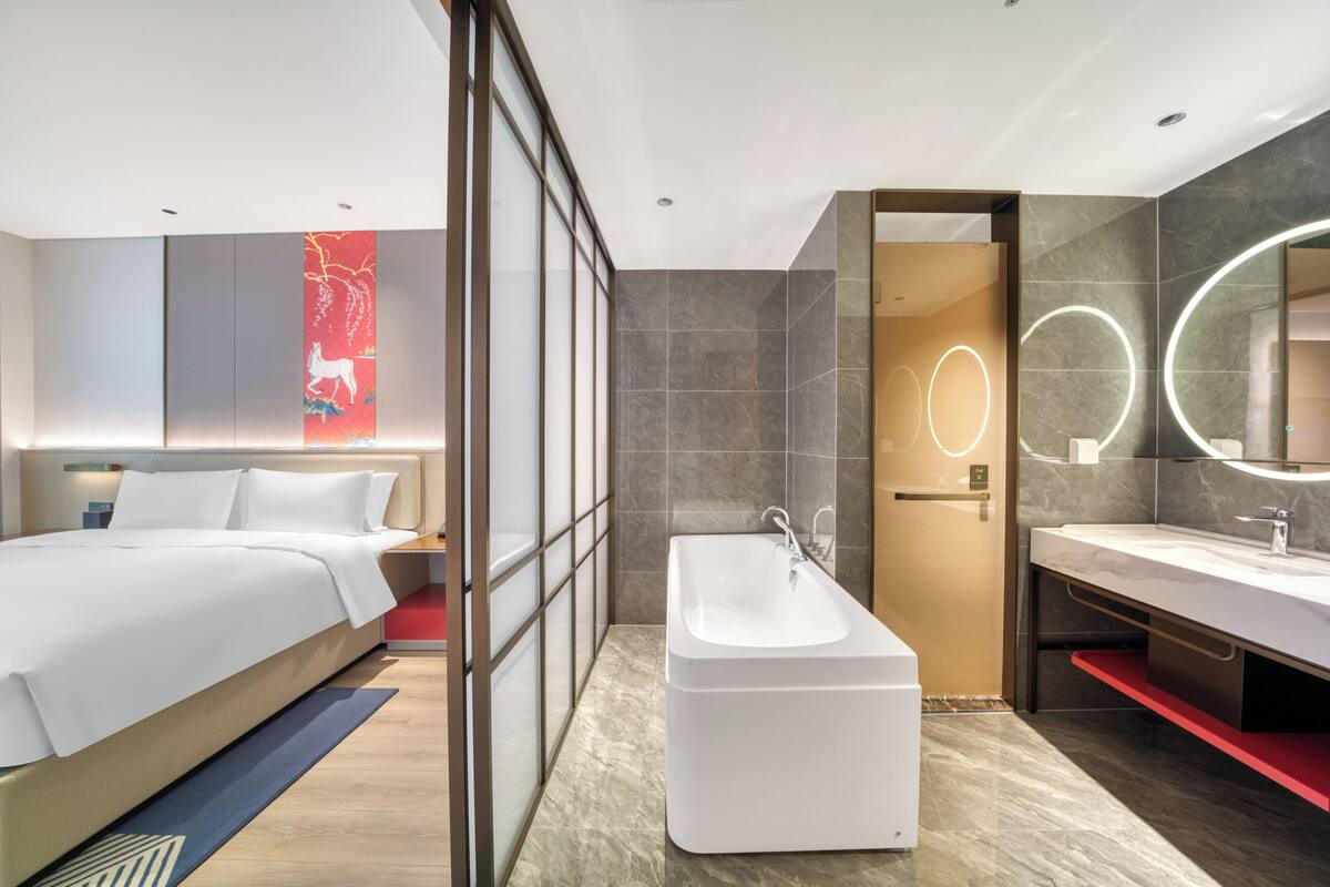 Ein modernes Hotelzimmer mit einem großen Bett, einem separaten Badezimmer mit einer Badewanne und einem großen Spiegel.