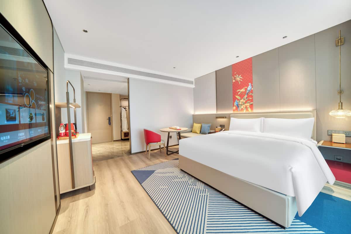 Ein modernes Hotelzimmer mit einem großen Bett, einem Schreibtisch, einem Stuhl und einem Fernseher.