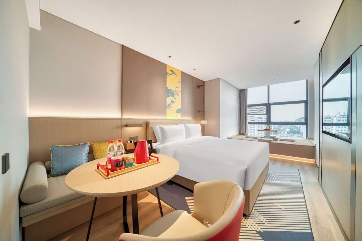 Ein modernes Hotelzimmer mit Bett, Sitzgelegenheit und Blick auf die Stadt.