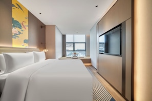 Quarto de hotel com uma cama grande, televisão, janela com vista para a cidade e um detalhe decorativo na parede.