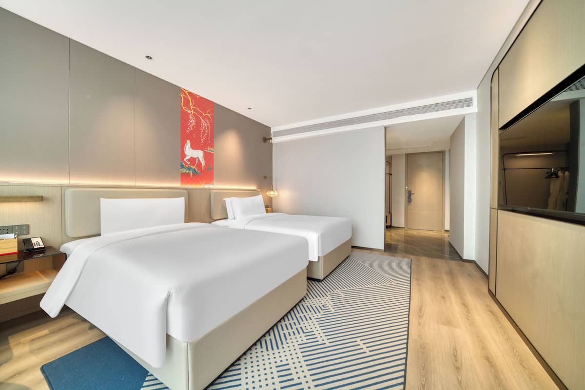 Ein modernes Hotelzimmer mit zwei Betten, einem großen Spiegel und Blick ins Badezimmer.