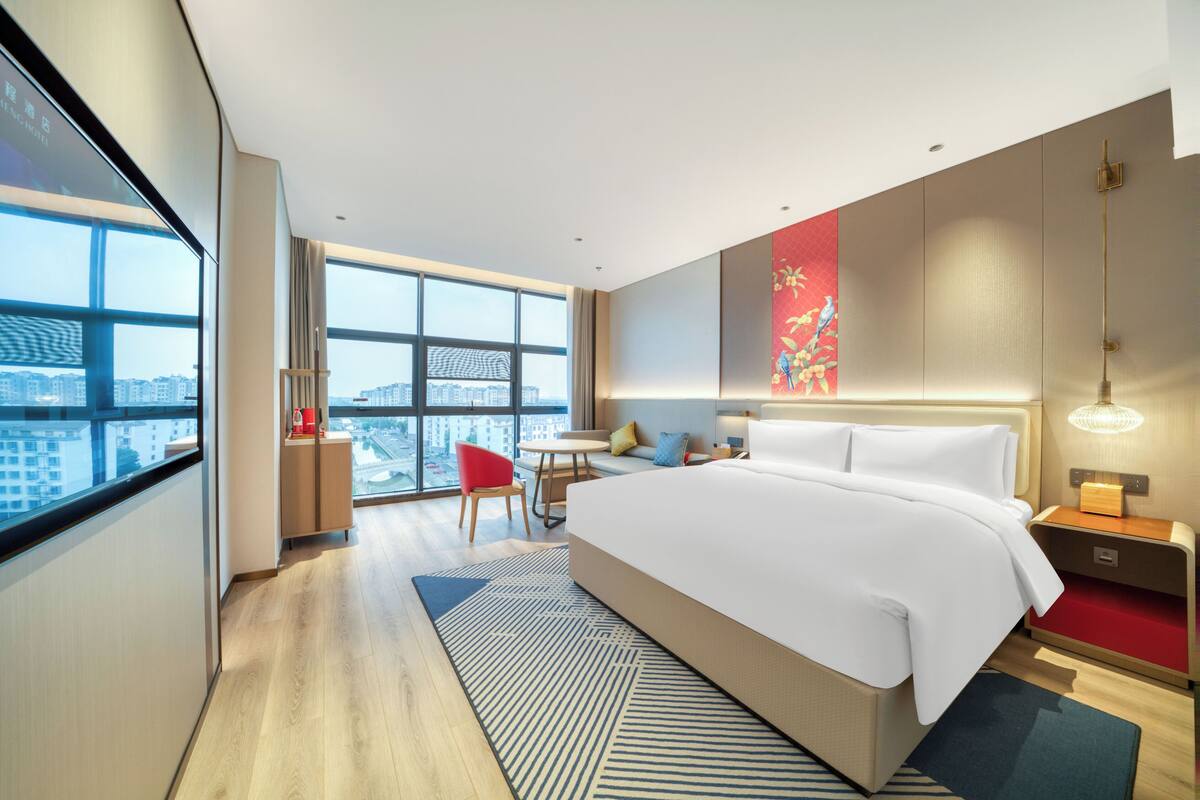 Ein modernes Hotelzimmer mit einem großen Bett, einem Schreibtisch, einem Sessel und Blick auf die Stadt.