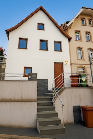 A two-story building with a white facade, brown trim, and a set of stairs leading to the entrance. - Small House Park Free at Street (Stuttgart)
