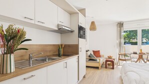Eine moderne Küche mit weißen Schränken, einer Holz Arbeitsplatte und einem Spülbecken. Es gibt eine Essecke mit Tisch und Stühlen, sowie ein Bett mit weißer Daunendecke.