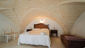 A bedroom with a stone ceiling, a bed with white linens, a bedside table, and a chair. - Anemone Studios - Double room with extra bed in Salento (Uggiano La Chiesa)