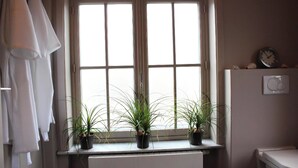 Un baño con ventana, dos plantas en macetas, un perchero para toallas, un reloj y un termostato.
