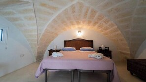 A bedroom with a stone ceiling, a bed with pillows and towels, a nightstand, and a small table. - Anemone Studios - Spacious room with extra bed near Otranto (Uggiano La Chiesa)