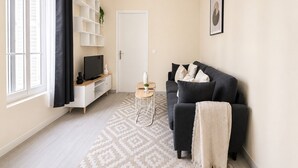 Ein Wohnzimmer mit einer Couch, einem Fernseher, einem weißen Bücherregal und einer Tür.