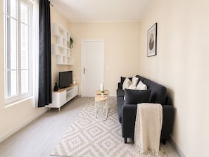 Een woonkamer met een bank, televisie, een witte boekenkast en een deur.