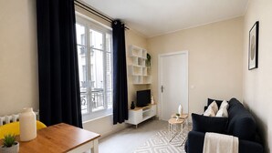 Ein modernes Wohnzimmer mit einem Holztisch, einem weißen Sessel, einem dunklen Sofa und einem Fernseher auf einem weißen Schrank.