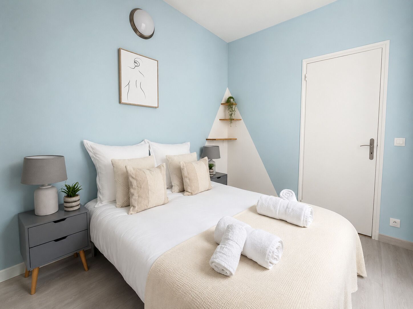 A bedroom with a bed, bedside tables, a lamp, a wall clock, a framed picture, and a door.
