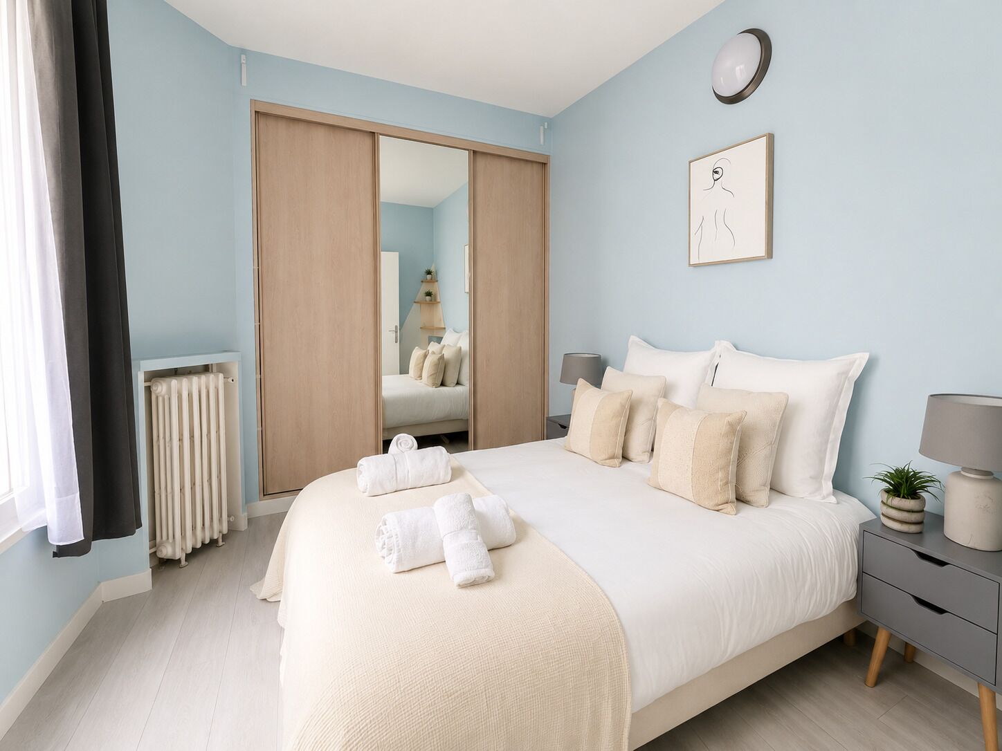 A bedroom with a bed, bedside tables, a radiator, a mirror, and a wall-mounted lamp.