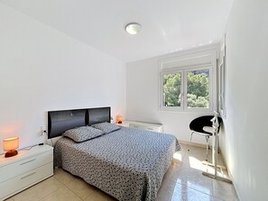 Ein Schlafzimmer mit Bett, Nachttischen, Schreibtisch, Stuhl, Fenster und Deckenleuchte.