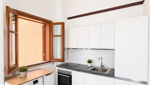 A compact kitchen with a washing machine, oven, sink, and wooden window frame. - Vacation home facing the sea in Scylla (Scilla)