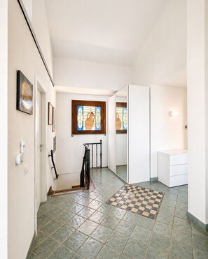 Um corredor com piso xadrez, escada, porta com corrimão e luminária na parede.