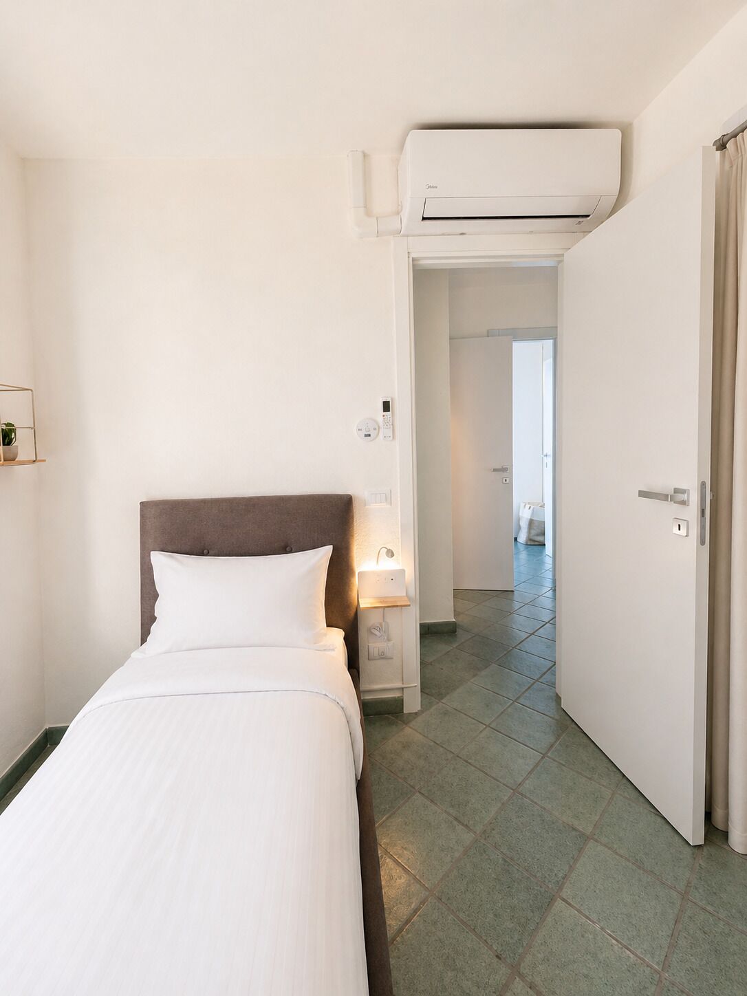 Une chambre d’hôtel comprenant un lit, une table de chevet, un climatiseur fixé au mur et une porte donnant sur une autre pièce.