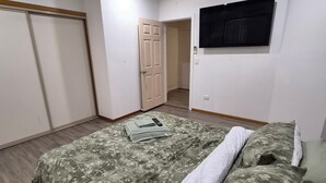 Een slaapkamer met een bed, een plafondventilator, een televisie en een deur.
