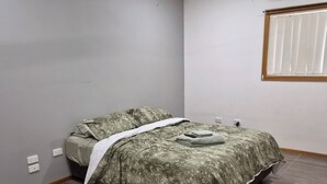 Een slaapkamer met een bed, een plafondventilator, een airconditioning en een raam met jaloezieën.