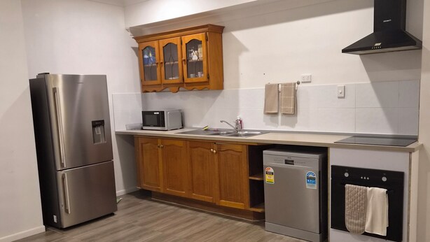 Een moderne keuken met een roestvrijstalen koelkast, houten kastjes, een magnetron, een vaatwasser en een plafondventilator.