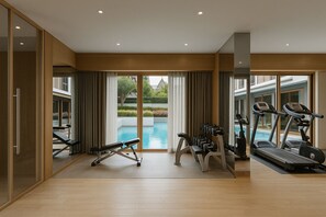 Ein großzügiges Hallenfitnessstudio mit Trainingsgeräten und Blick auf einen Pool, ausgestattet mit Holzböden.