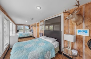 Ein Zimmer mit zwei Betten, Holzwänden, einem aufgehängten Hirschgeweih und einem kleinen Tisch mit Ventilator.