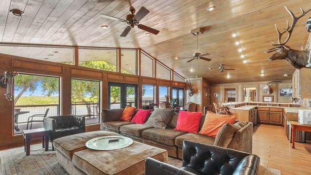 A spacious living area with a large window, a ceiling fan, and a mounted deer head. - Casa Arroyo Upper Level - Dock, Sleeps 14 (Arroyo City)