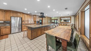 A kitchen with wooden cabinets, a stainless steel refrigerator, a large island with stools, and a dining table with chairs. - Casa Arroyo Upper Level - Dock, Sleeps 14 (Arroyo City)