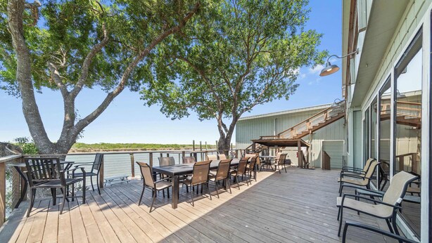 Un terrazzo in legno con mobili da esterno, un albero grande e un edificio con una scala.