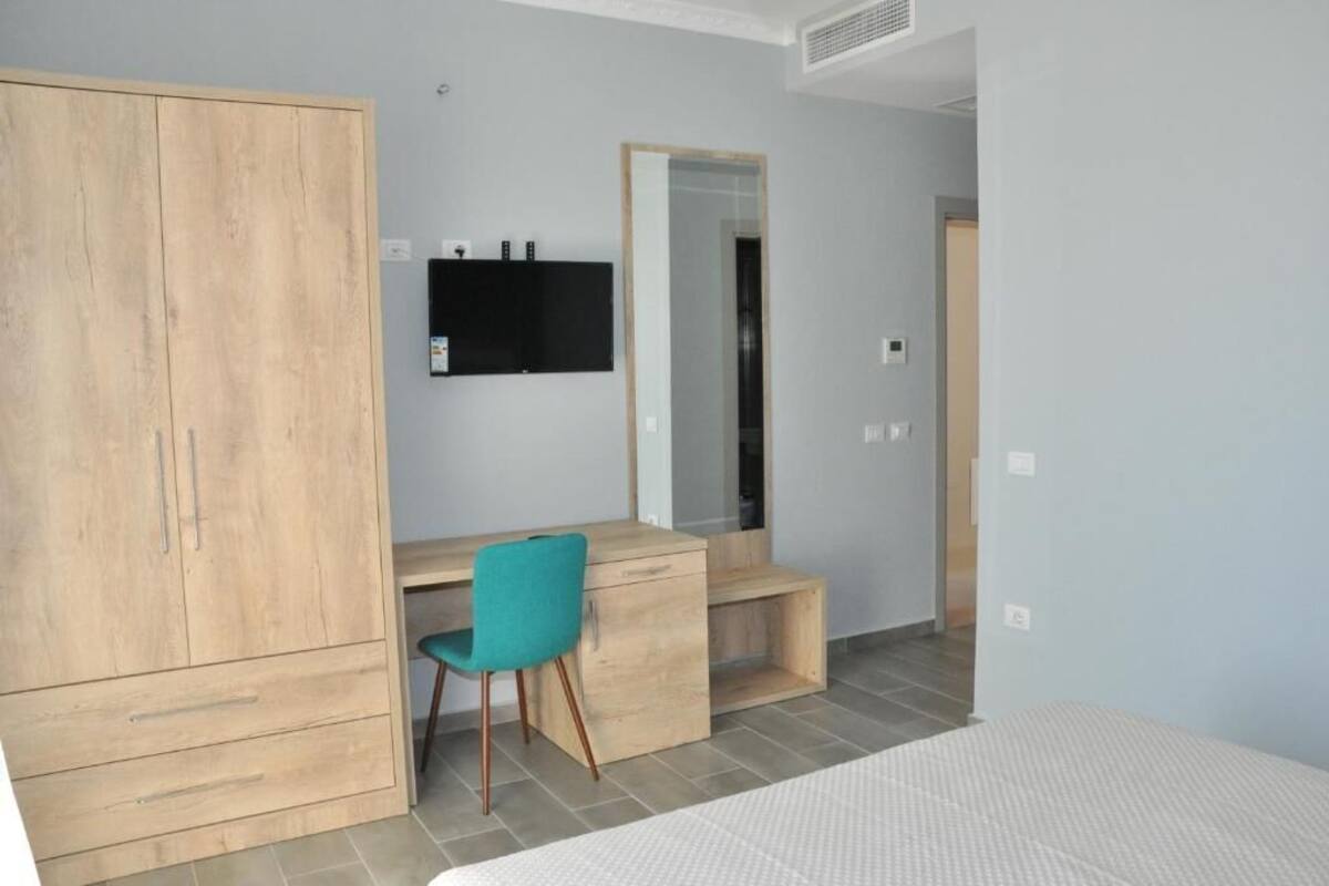 Un dormitorio con cama, armario de madera, escritorio con silla, espejo y televisión.