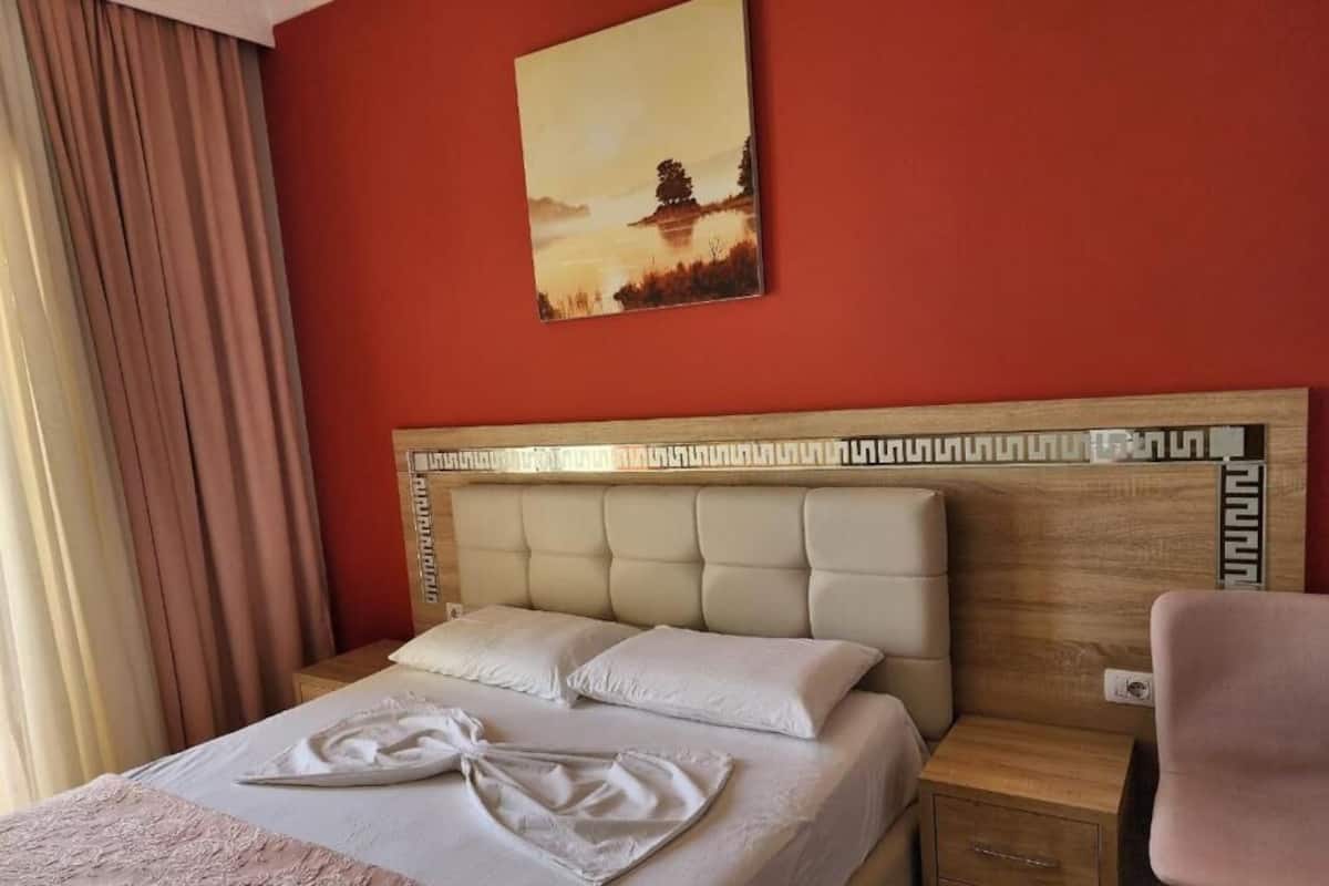 Habitación de hotel con cama, cabecera, mesita de noche, una silla y un cuadro en la pared.
