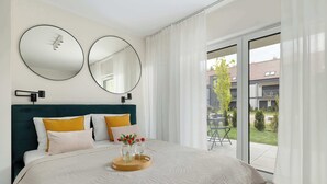 Ein Schlafzimmer mit einem Bett, zwei Wandspiegeln, einem Nachttisch mit Tablett und Blick auf einen Außenbalkon.