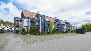 Ein modernes Mehrfamilienhaus mit mehreren Balkonen, einer gepflasterten Auffahrt und blauem Himmel.