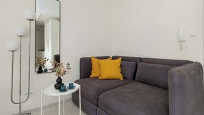 Ein modernes Wohnzimmer mit einem grauen Sofa, einem kleinen weißen Beistelltisch, einem Spiegel und einer Stehlampe.