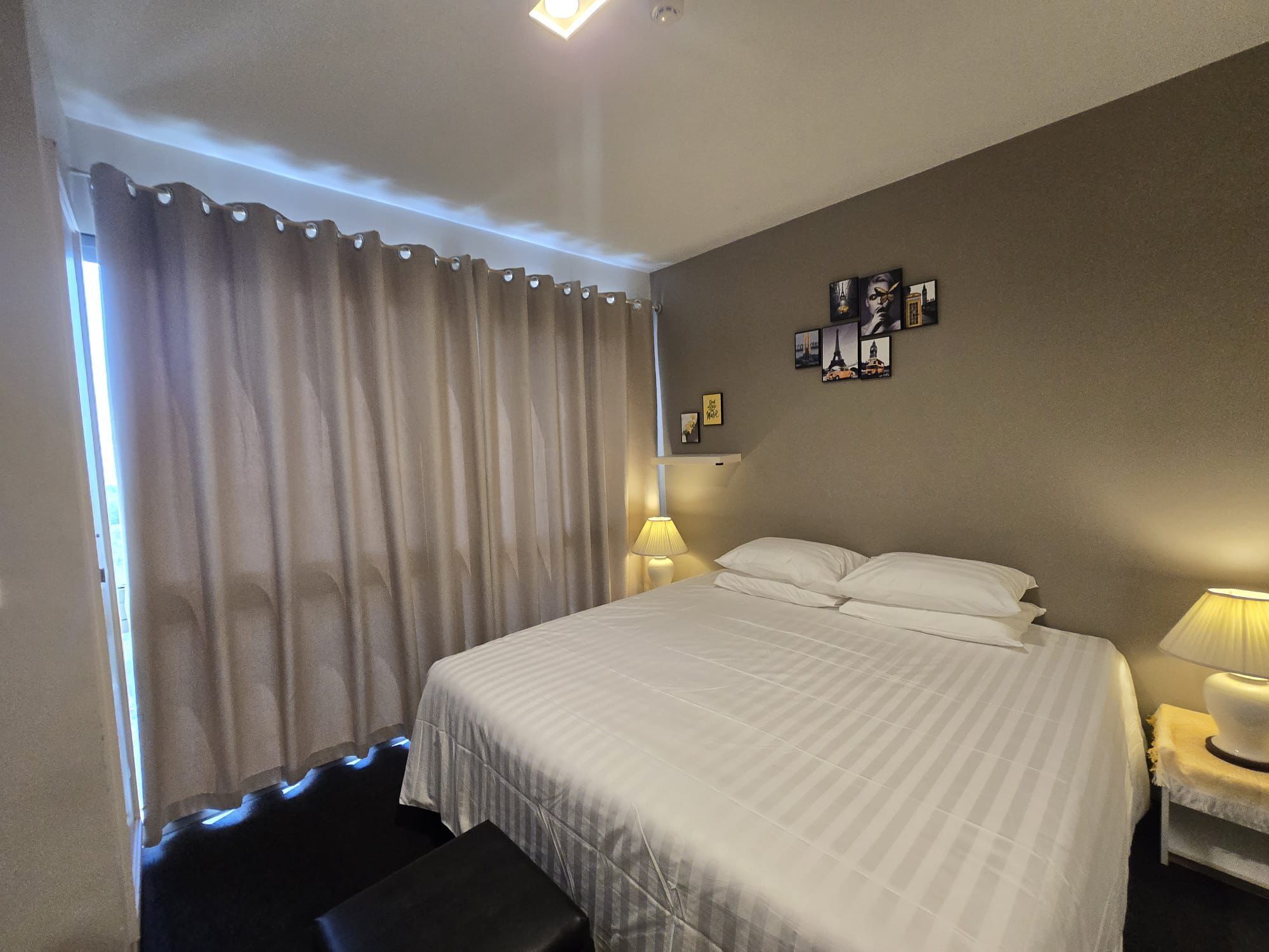 Hotelkamer met een groot bed, twee bedlampen, een raam met gordijnen en een muur met ingelijste foto's.