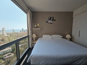 Ein Hotelzimmer mit einem großen Bett, zwei Nachttischlampen, Blick auf die Stadt und einer Wand mit gerahmten Bildern.