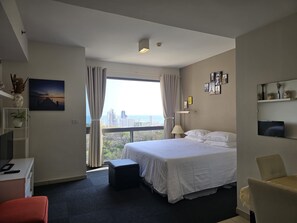 Ein Hotelzimmer mit Bett, Schreibtisch, Stuhl, Fernseher und Blick auf die Stadt.