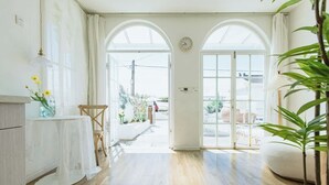 Una habitación amplia con suelo de madera, una mesa blanca con un florero y un amplio arco que da al exterior.