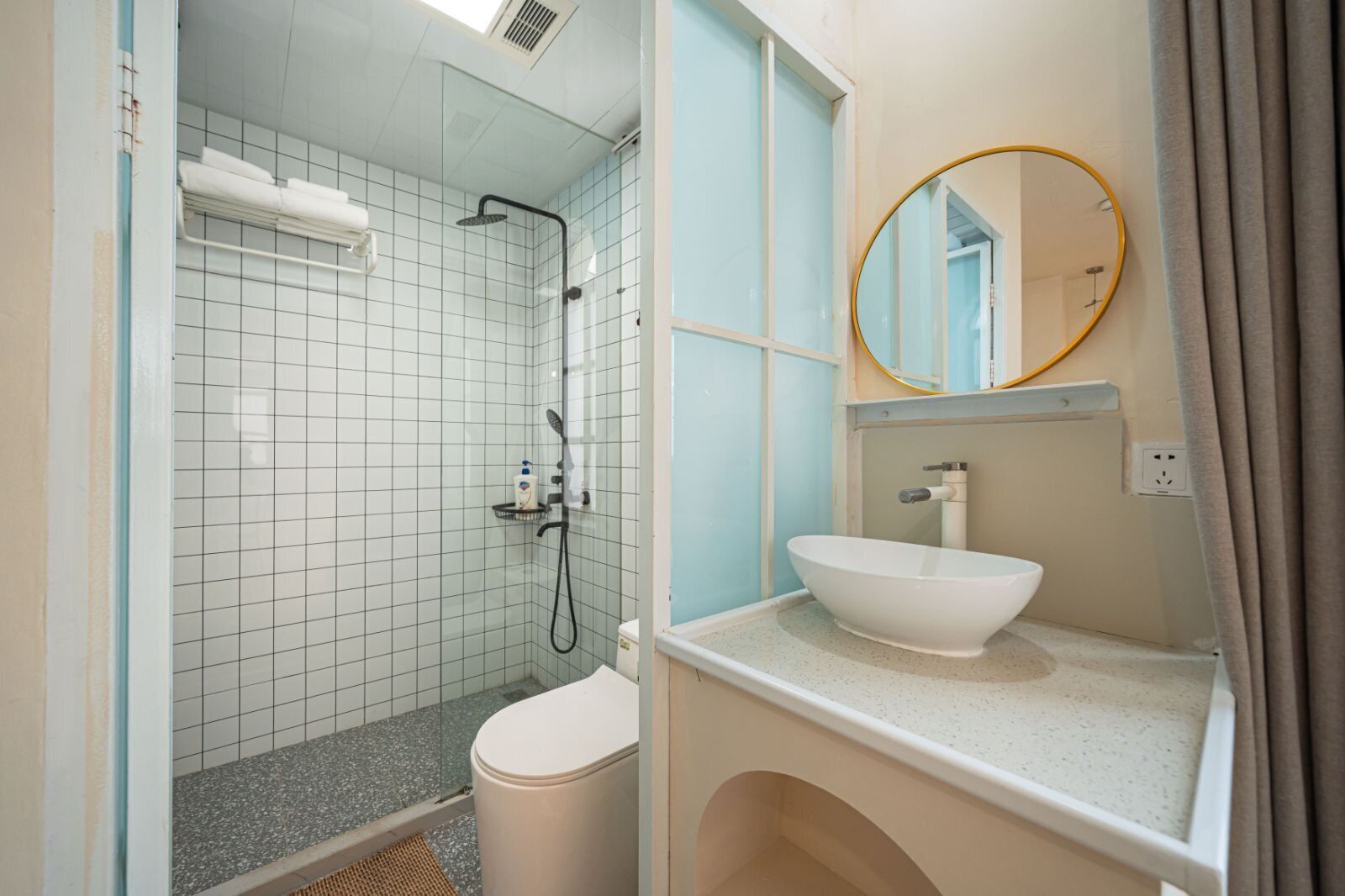 A bathroom with a glass-enclosed shower, a white sink, and a round mirror.