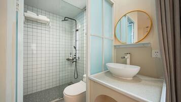 A bathroom with a glass-enclosed shower, a white sink, and a round mirror.
