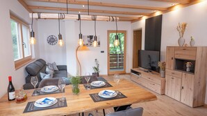 A dining area with a wooden table set for four, a sofa, and a TV in the background. - Modern apartment with mountain view (Chiusa)
