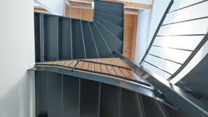 A spiral staircase with a wooden floor and metal railings, leading to an upper level with a sloped ceiling and wooden paneling. - Modern apartment with mountain view (Chiusa)