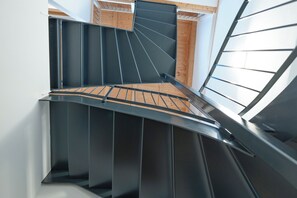 A spiral staircase with a wooden floor and metal railings, leading to an upper level with a sloped ceiling and wooden paneling. - Modern apartment with mountain view (Chiusa)